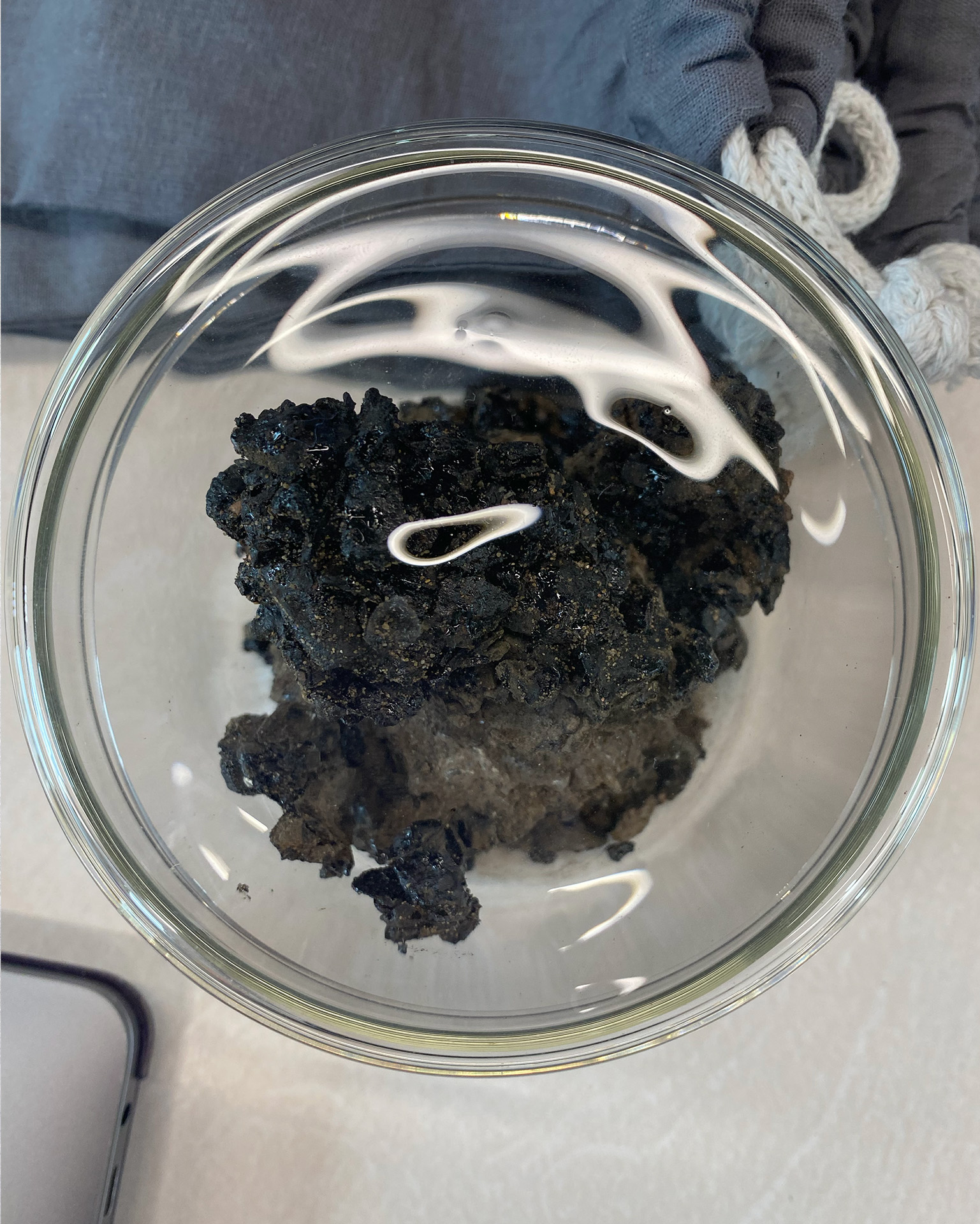 Photo of a dark and glitering structure within a glass. The structure is as big as a fist, seems like a stone with an irregular surface at first, but is more brittle. The structure is: asphalt.